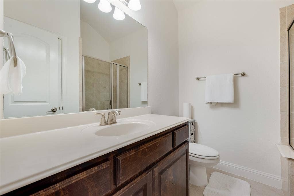 2408 Brisbane Lane, Plano, TX 75075 Vanity with an integrated sink, brushed nickel faucet, wood-finish cabinetry, and a shower with a glass enclosure