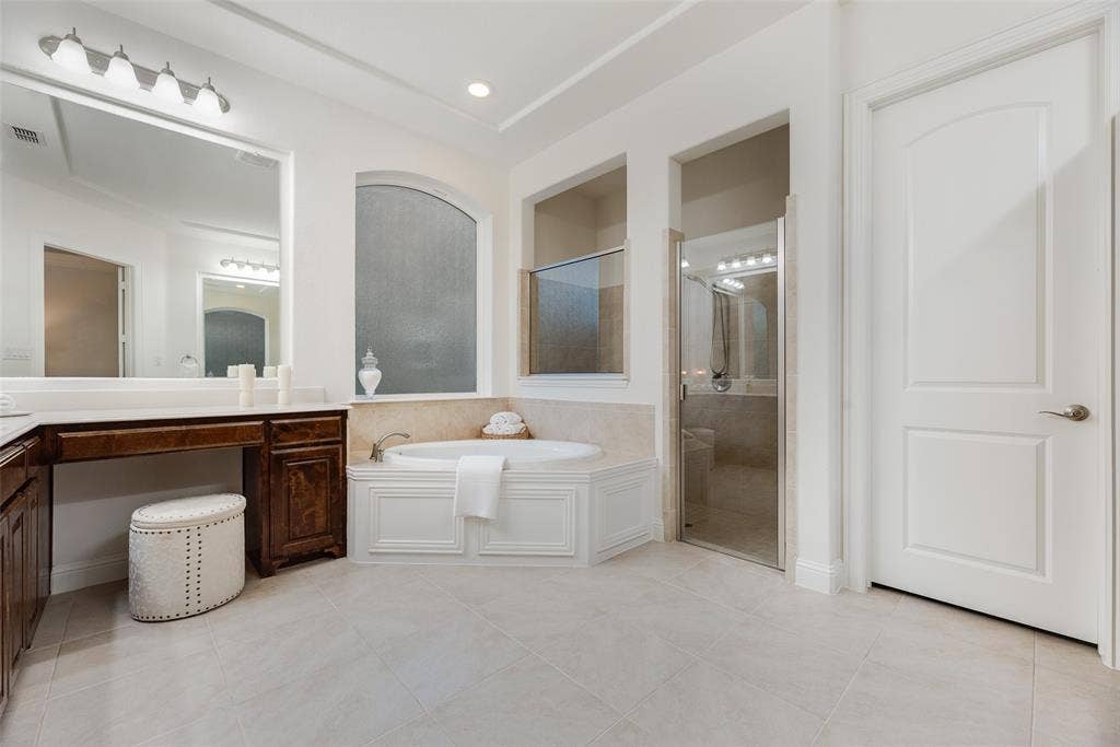 2408 Brisbane Lane, Plano, TX 75075 Corner soaking tub, separate shower with glass enclosure, dual vanity with wood-finish cabinetry, and neutral tile flooring