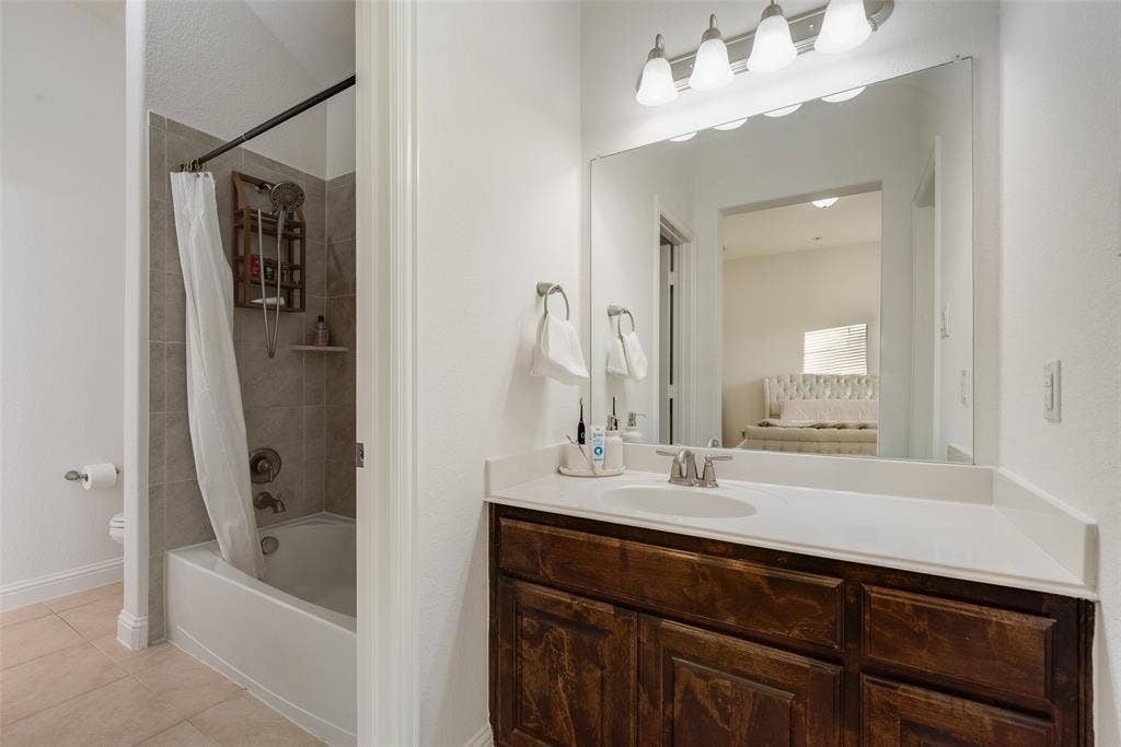 2408 Brisbane Lane, Plano, TX 75075 Jack and Jill Bathroom. Bathtub with tiled shower surround, single vanity with integrated sink, dark wood-finish cabinetry, and overhead vanity lighting