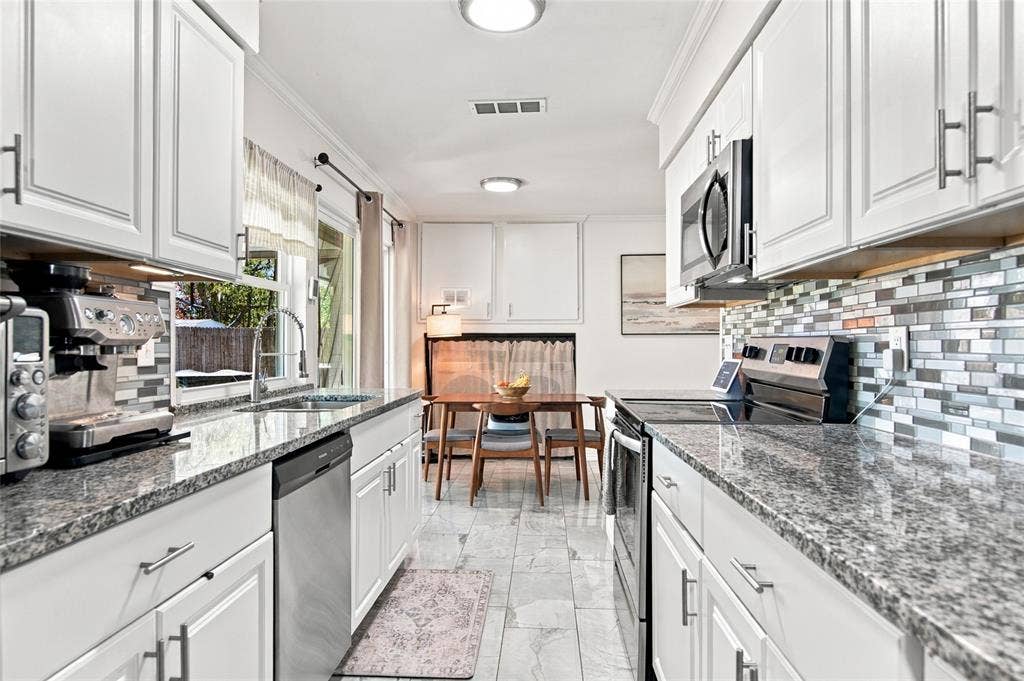 4720 Kyle Drive, Balch Springs, TX 75180 White cabinetry with brushed nickel hardware, granite countertops, stainless steel appliances, mosaic tile backsplash, and tile flooring