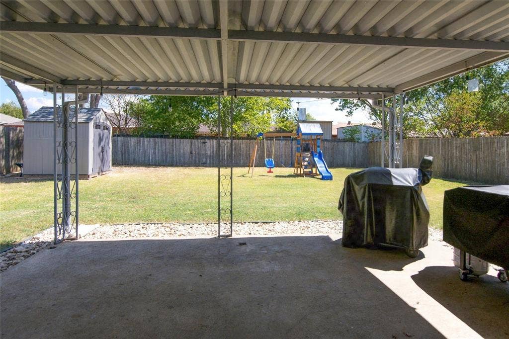 4720 Kyle Drive, Balch Springs, TX 75180 Covered concrete patio with decorative metal supports, overlooking a grassy yard with a privacy fence and a storage shed