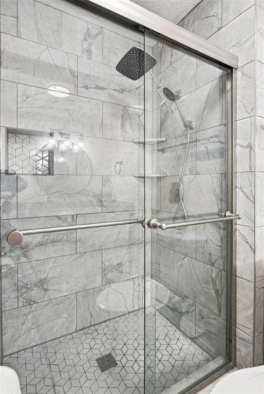 4720 Kyle Drive, Balch Springs, TX 75180 Glass-enclosed shower with a rainfall showerhead, handheld sprayer, geometric tile flooring, and large format wall tiling