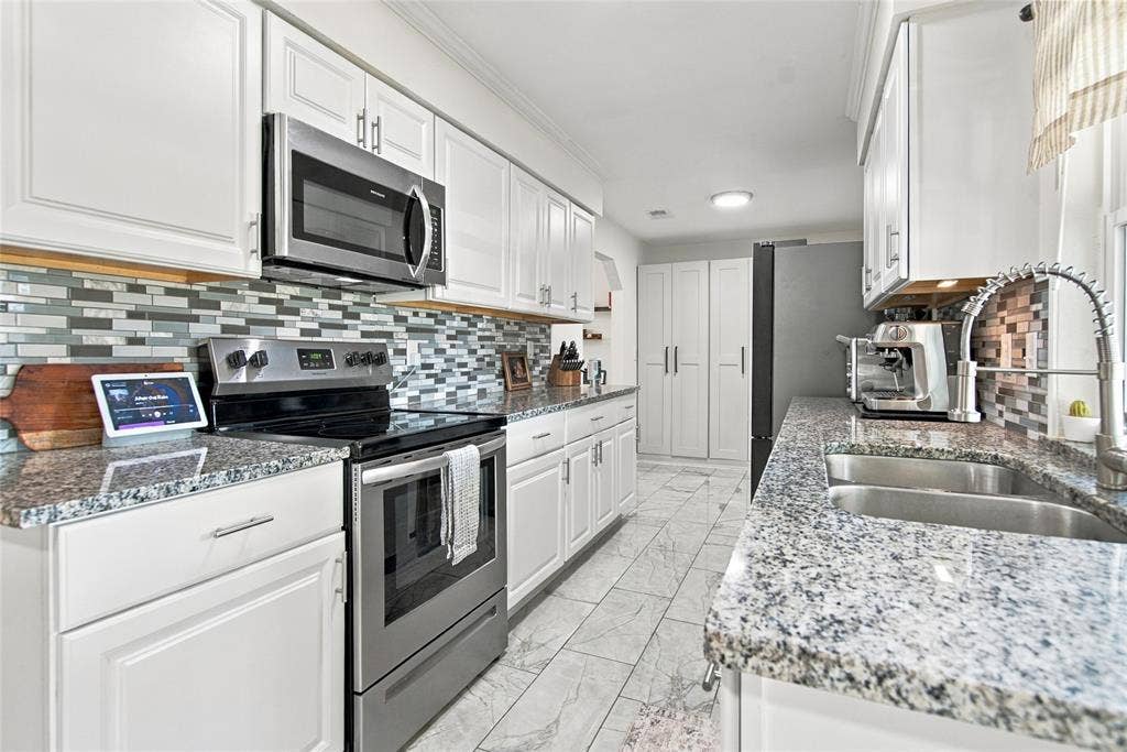 4720 Kyle Drive, Balch Springs, TX 75180 White cabinetry, stainless steel appliances, mosaic tile backsplash, double basin sink, and stone-finish countertops