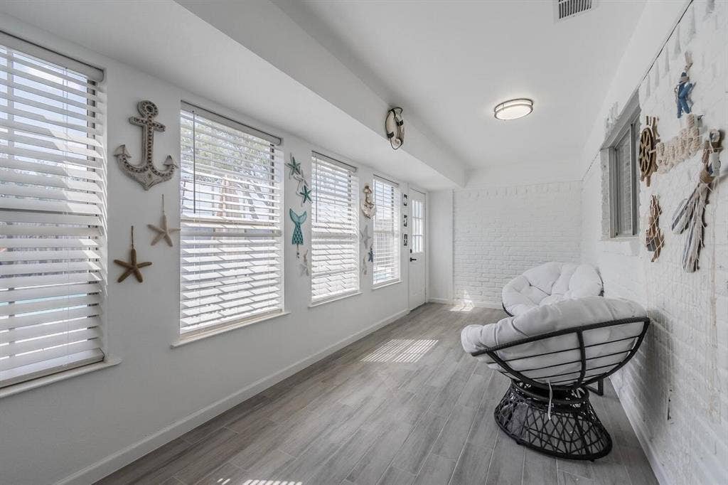 White painted brick wall, recessed lighting, wood-finish flooring, multiple windows with blinds, and a white door with frosted glass panes