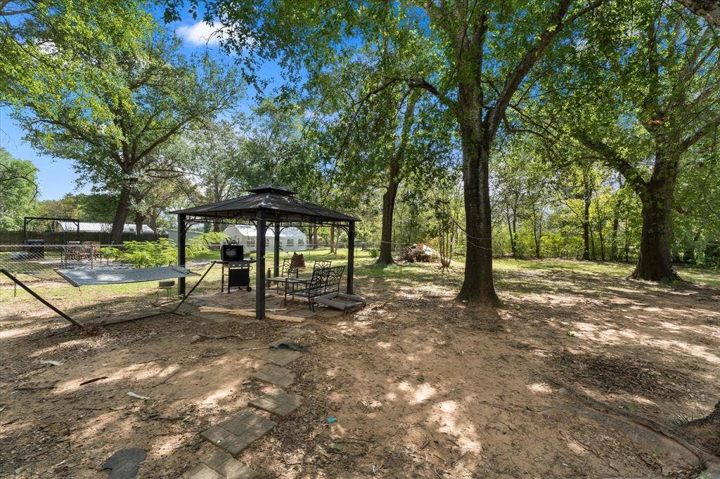 402 E Cook Street, Eustace, TX 75124 LARGE LOT with mature shade trees, a metal-framed gazebo, and a stone paver pathway