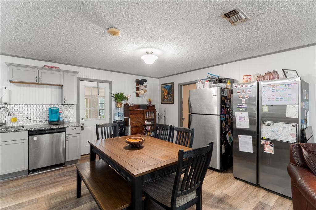 402 E Cook Street, Eustace, TX 75124 Kitchen area featuring gray cabinetry, stone-finish countertops, a hexagonal tile backsplash, stainless steel appliances, and wood-finish flooring