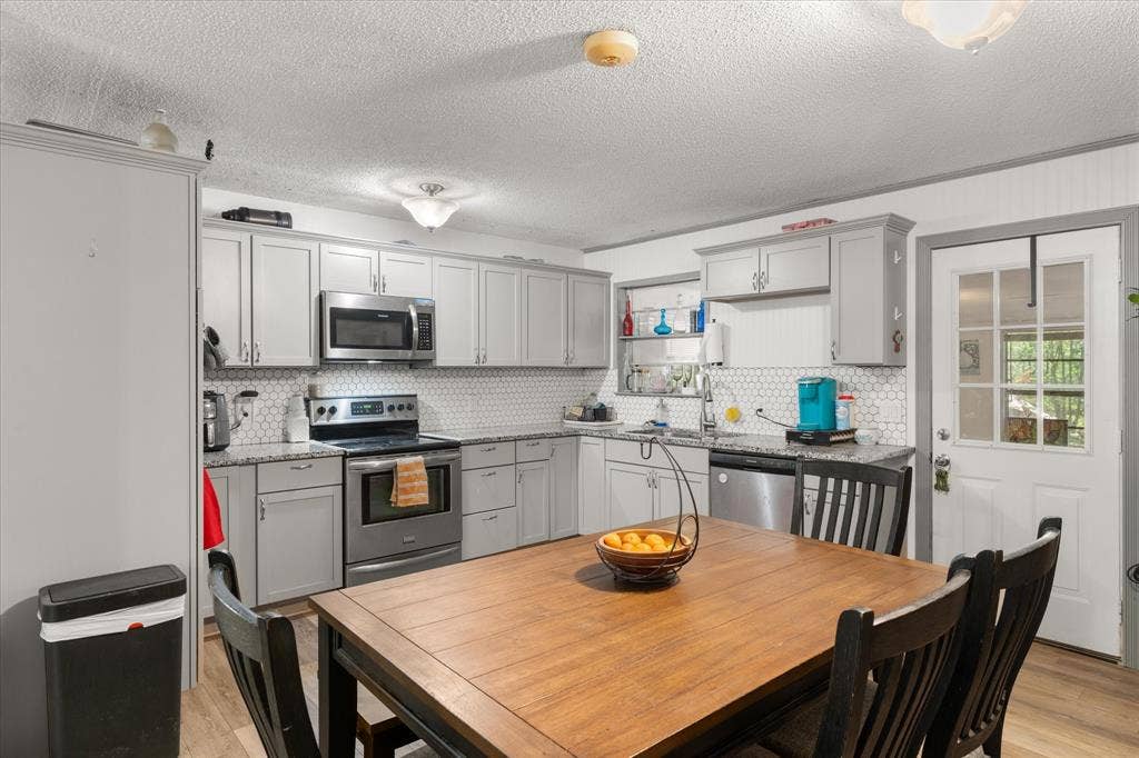 402 E Cook Street, Eustace, TX 75124 Kitchen featuring shaker cabinetry, stainless steel appliances, speckled stone-finish countertops, and a white hexagonal tile backsplash