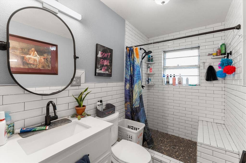 402 E Cook Street, Eustace, TX 75124 Fully remodeled Bathroom featuring a white vanity with an integrated rectangular sink, matte black faucet, oval wall-mounted mirror, white subway tile walls, and a walk-in shower with stone flooring