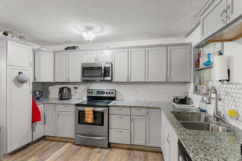 402 E Cook Street, Eustace, TX 75124 Kitchen featuring stone-finish countertops, stainless steel appliances, a white hexagonal tile backsplash, and wood-finish flooring