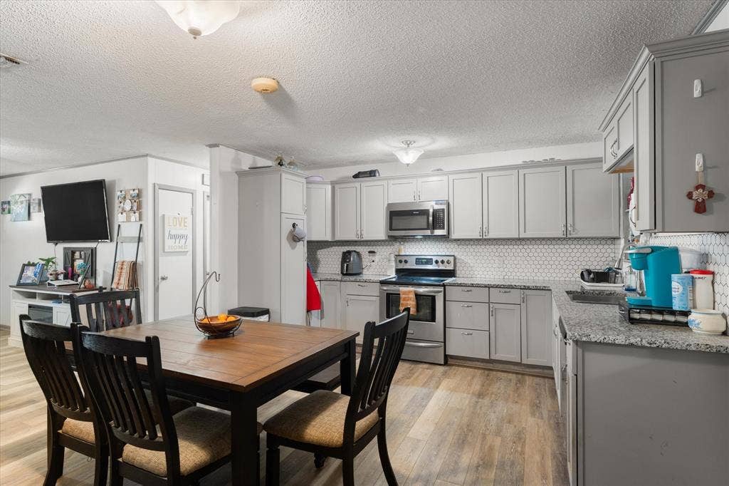 402 E Cook Street, Eustace, TX 75124 Kitchen featuring grey cabinetry, stone-finish countertops, stainless steel appliances, hexagonal tile backsplash, and wood-finish flooring