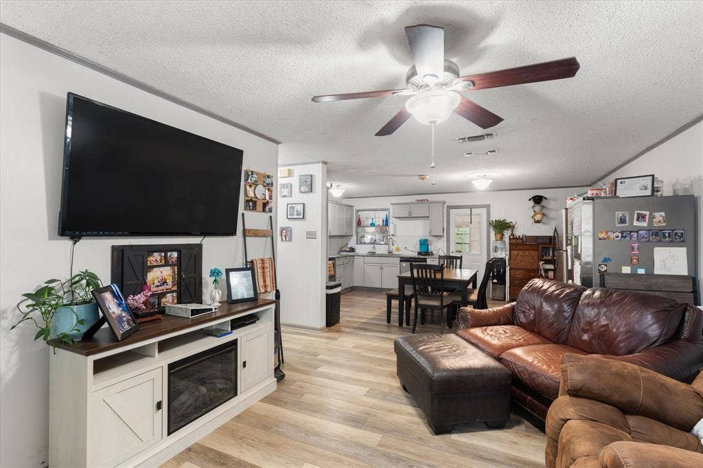 402 E Cook Street, Eustace, TX 75124 Open-concept living space featuring wood-finish flooring, ceiling fan with integrated lighting, and built-in electric fireplace console