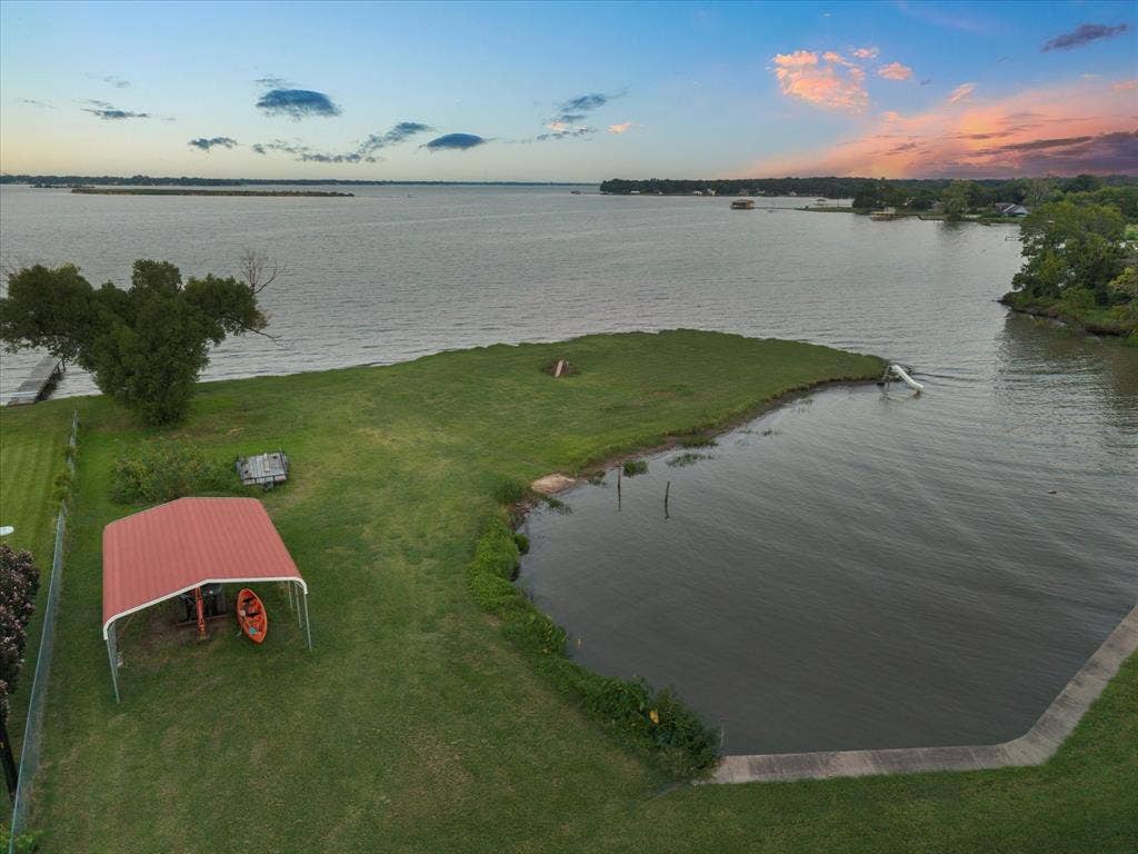 308 Causeway Cove, Seven Points, TX 75143 Expansive waterfront property featuring a manicured lawn, an extended pier, a red metal carport, and a concrete bulkhead