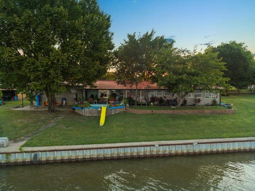 308 Causeway Cove, Seven Points, TX 75143 Waterfront property with a corrugated metal retaining wall, expansive green lawn, mature trees, and an elevated wooden deck