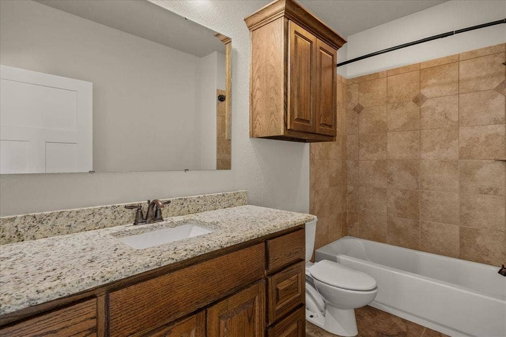 3674 County Road 2142, Caddo Mills, TX 75135 Bathroom featuring a vanity with an integrated sink, a speckled countertop, wood-finish cabinetry, and a shower-tub combination with tiled walls