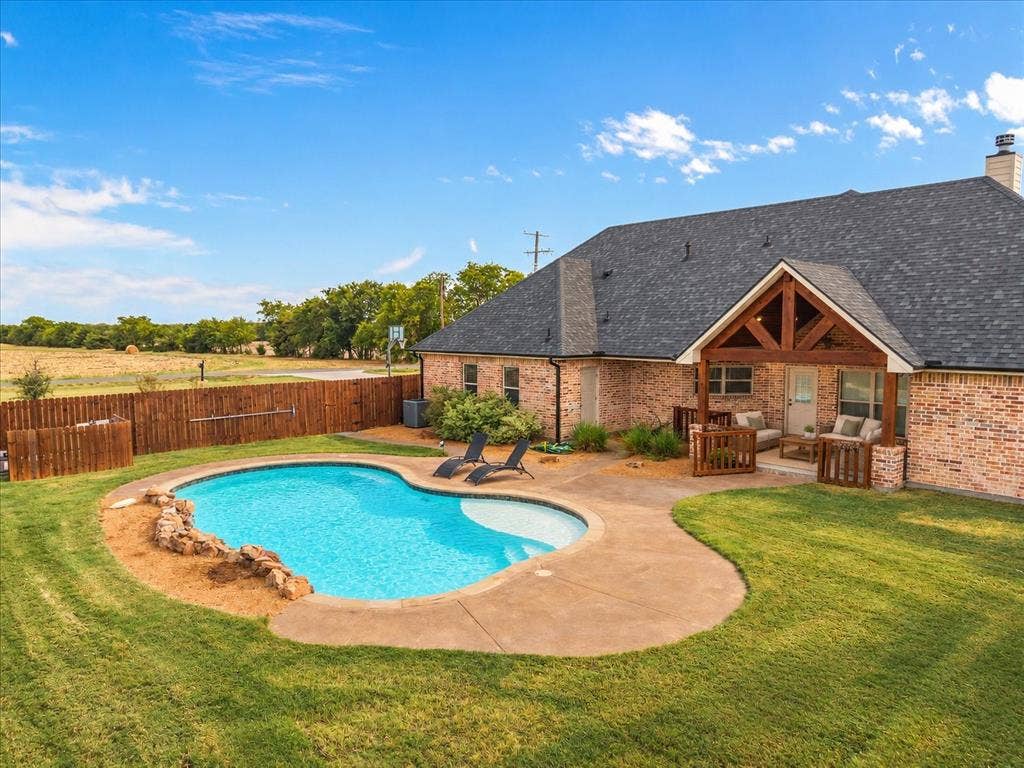 3674 County Road 2142, Caddo Mills, TX 75135 Brick exterior with a gabled roofline, a built-in covered patio, and a fenced backyard featuring a swimming pool with concrete decking