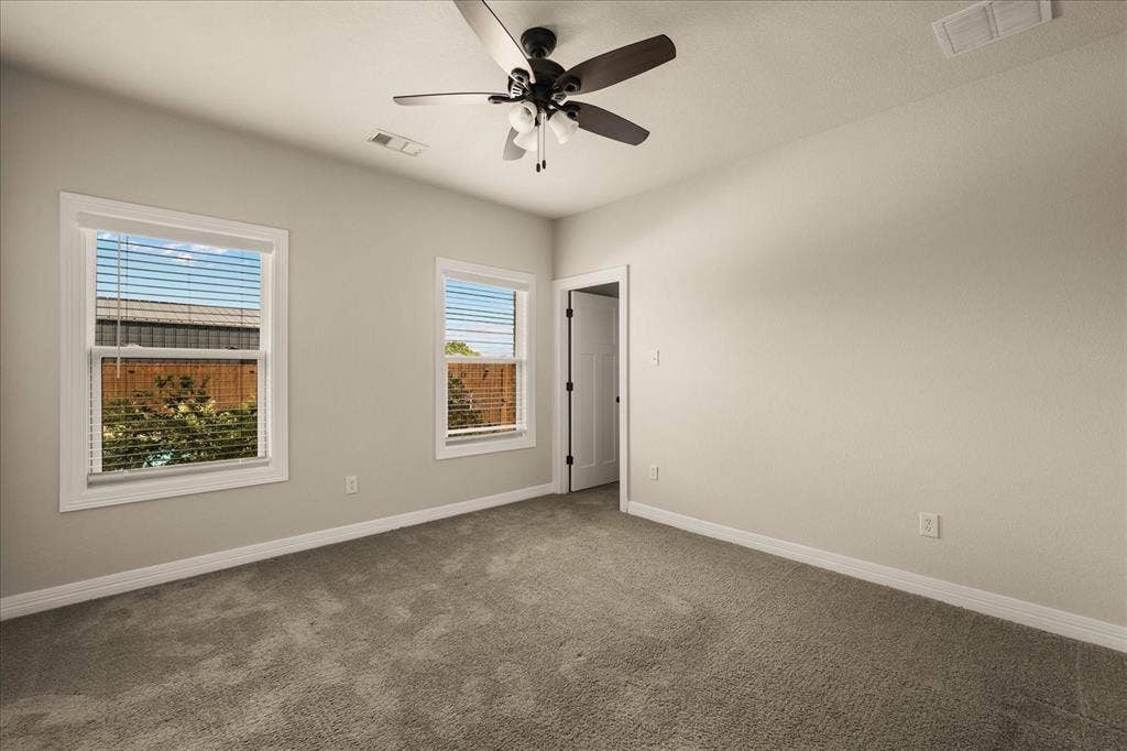 3674 County Road 2142, Caddo Mills, TX 75135 Spacious room featuring neutral carpeting, two double-hung windows with blinds, a ceiling fan with integrated lighting, and a white interior door