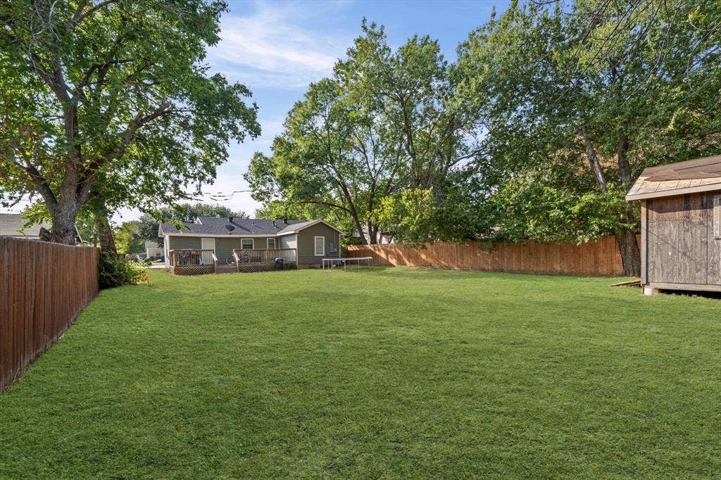 3605 Rolando Avenue, Waco, TX 76711 Spacious fenced backyard featuring a wood privacy fence, mature trees, a detached storage shed, and a rear deck