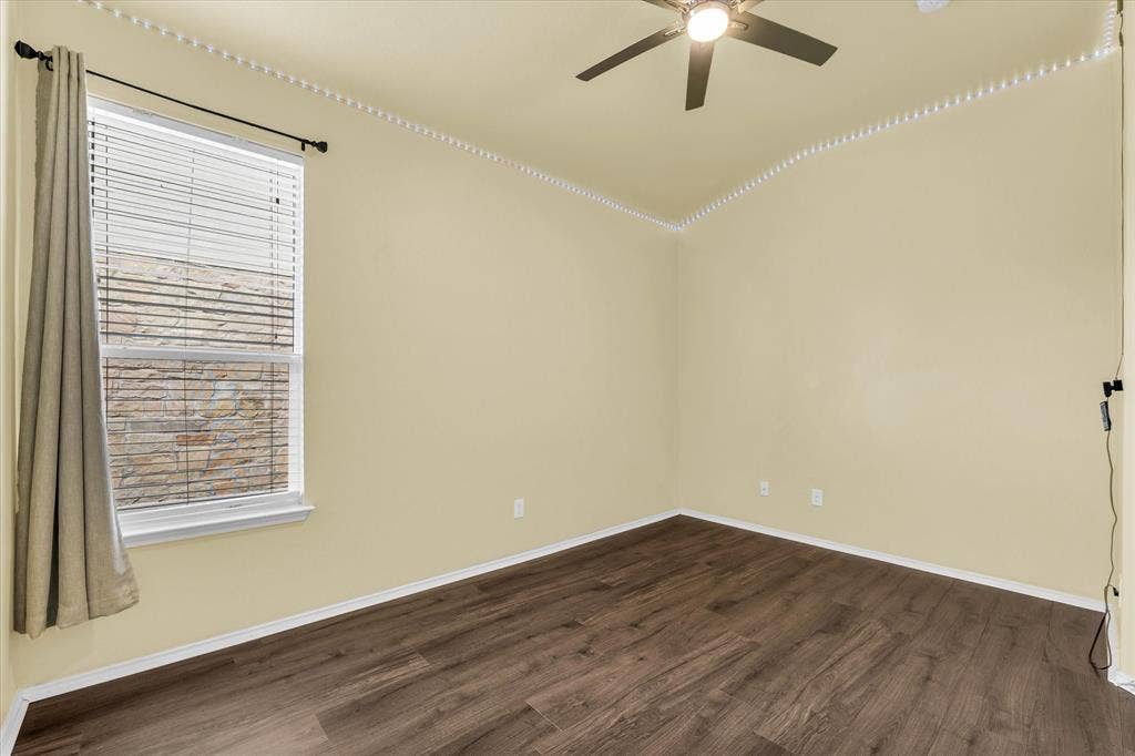 6621 Burling Street, Waco, TX 76712 Wood-finish flooring with crisp white baseboards, a single window with blinds and a drapery rod, and a ceiling fan