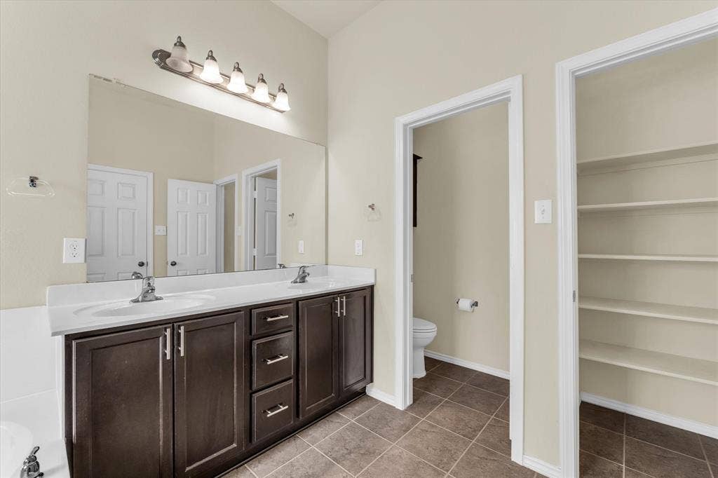 6621 Burling Street, Waco, TX 76712 Dual vanity with white countertop, dark wood-finish cabinetry, a large wall-mounted mirror, and tile flooring