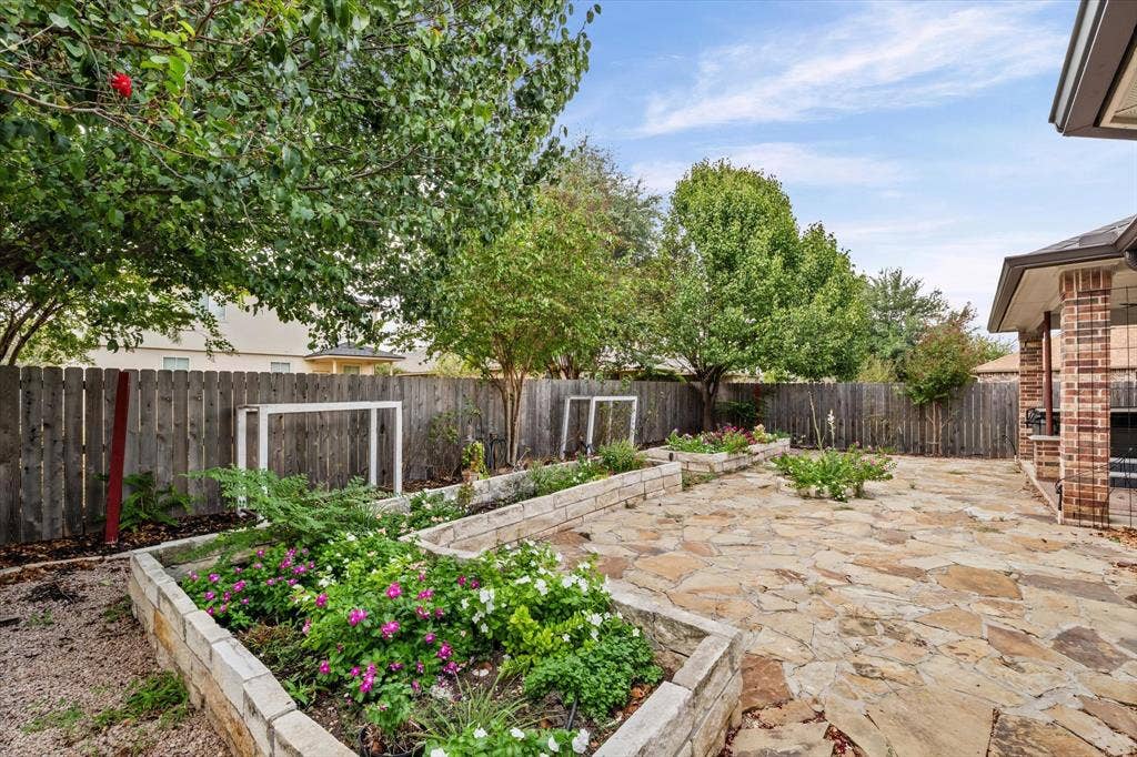 6621 Burling Street, Waco, TX 76712 Expansive backyard featuring a natural stone patio, raised garden beds with established plantings, a wooden privacy fence, and mature trees