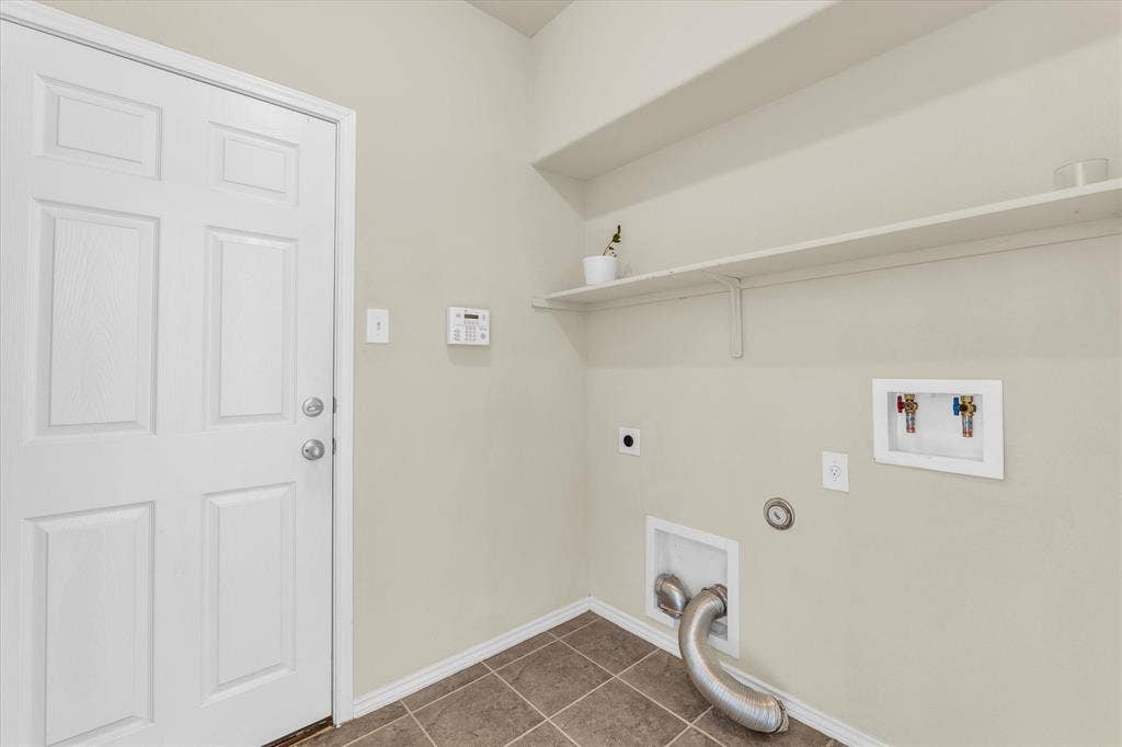 6621 Burling Street, Waco, TX 76712 Utility space featuring tiled flooring, a white paneled door, wall-mounted shelving, and laundry hookups