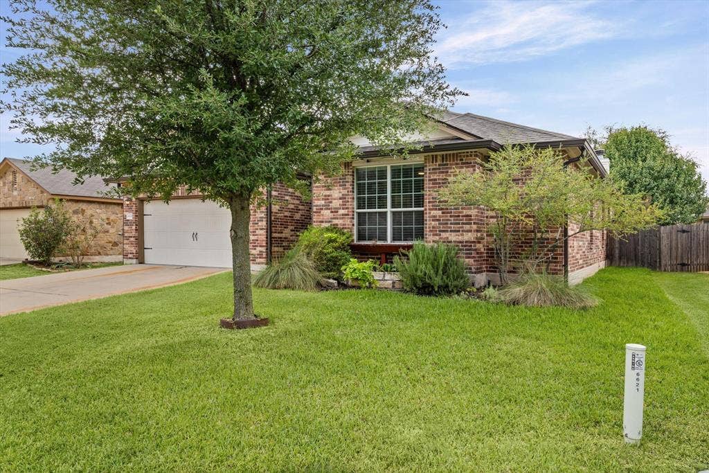 6621 Burling Street, Waco, TX 76712 Brick exterior with a mature tree, an attached garage, a manicured lawn, and established landscaping