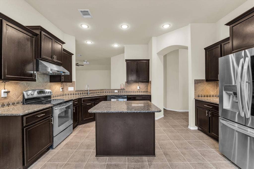 6621 Burling Street, Waco, TX 76712 Kitchen featuring dark wood-finish cabinetry, granite countertops, a tiled backsplash, stainless steel appliances, and a central island