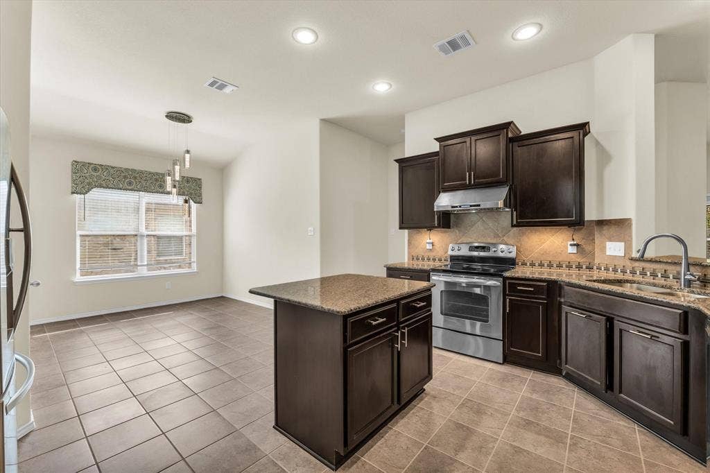 6621 Burling Street, Waco, TX 76712 Kitchen featuring dark wood cabinetry, stainless steel appliances, a center island, and tile flooring