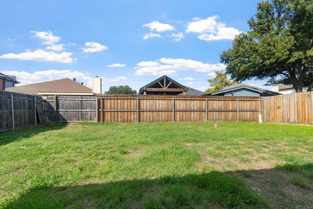 Backyard featuring an expansive lawn, full-perimeter wood fencing, and mature trees