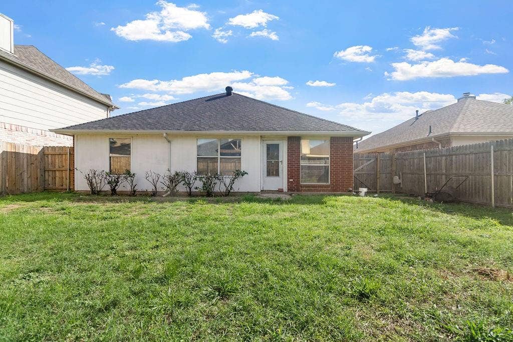 Rear exterior featuring a brick and stucco facade, a hip roof, and a fenced-in grass backyard