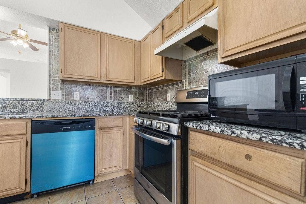 Kitchen featuring wood cabinetry, stone-finish countertops, decorative tile backsplash, stainless steel gas range, and ceramic tile flooring