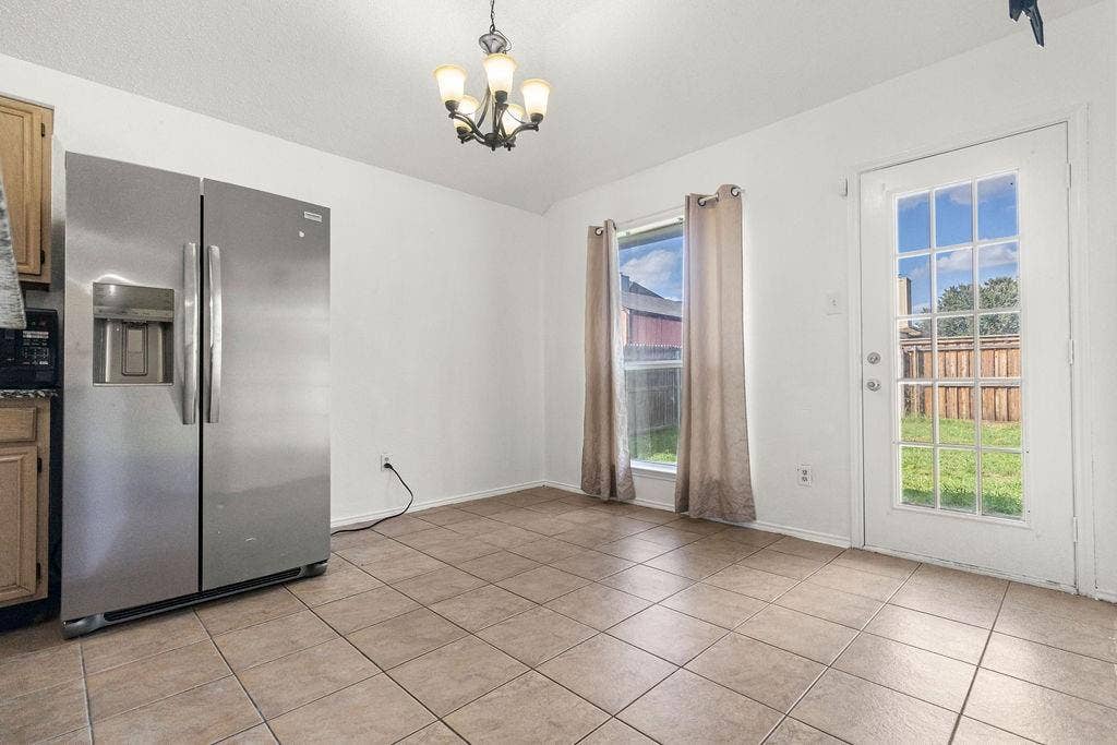 Ceramic tile flooring, stainless steel side-by-side refrigerator, multi-light chandelier, and a glass-paneled exterior door
