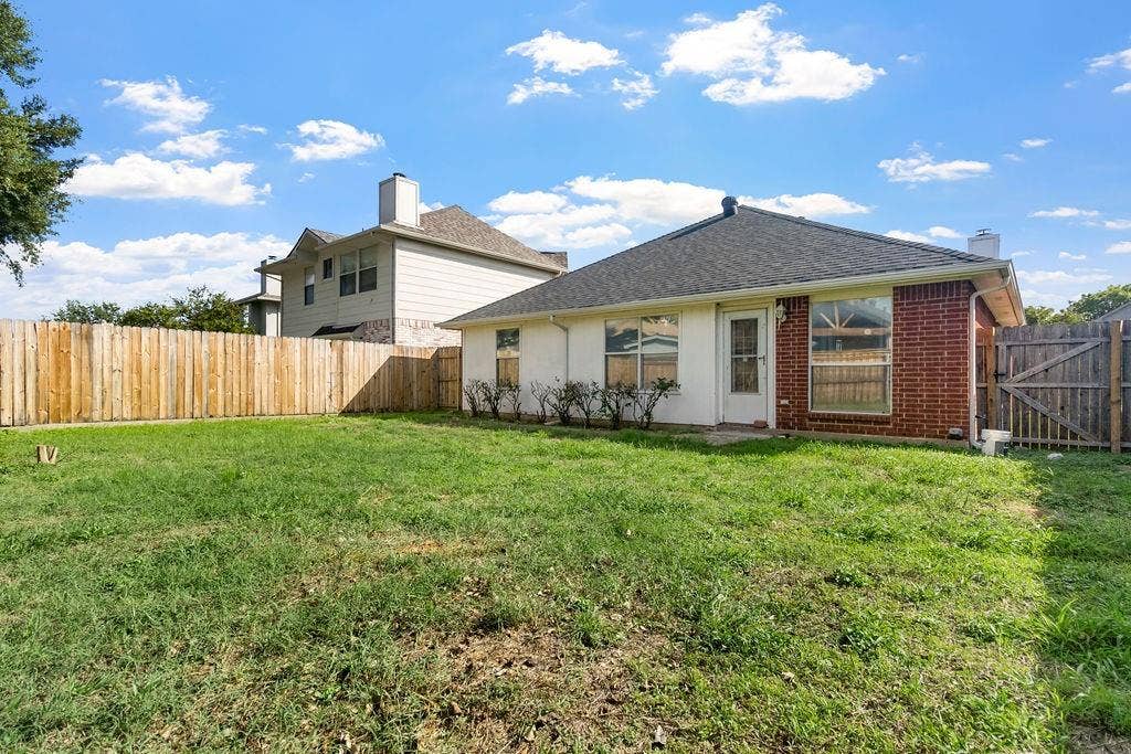 Backyard featuring a grass lawn, full-perimeter wood fencing, brick and stucco exterior, and a hip roofline