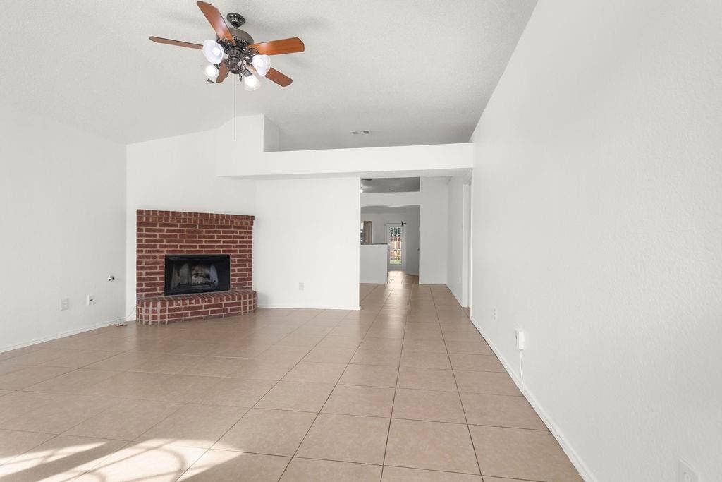 Living area featuring tile flooring, vaulted ceilings, a brick fireplace, and a ceiling fan with integrated lighting