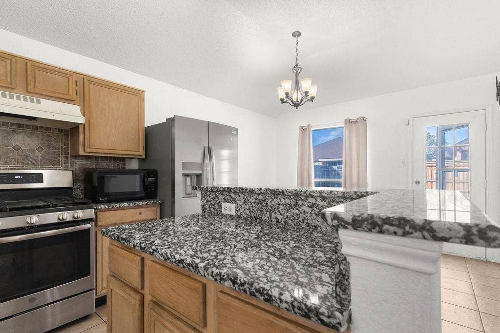Kitchen featuring stone countertops, raised breakfast bar, stainless steel appliances, wood cabinetry, and tile flooring