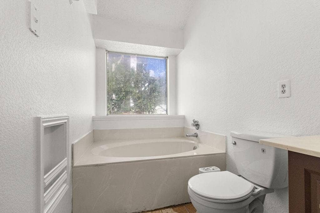 Oval soaking tub featuring an integrated surround, recessed wall niche, and large window