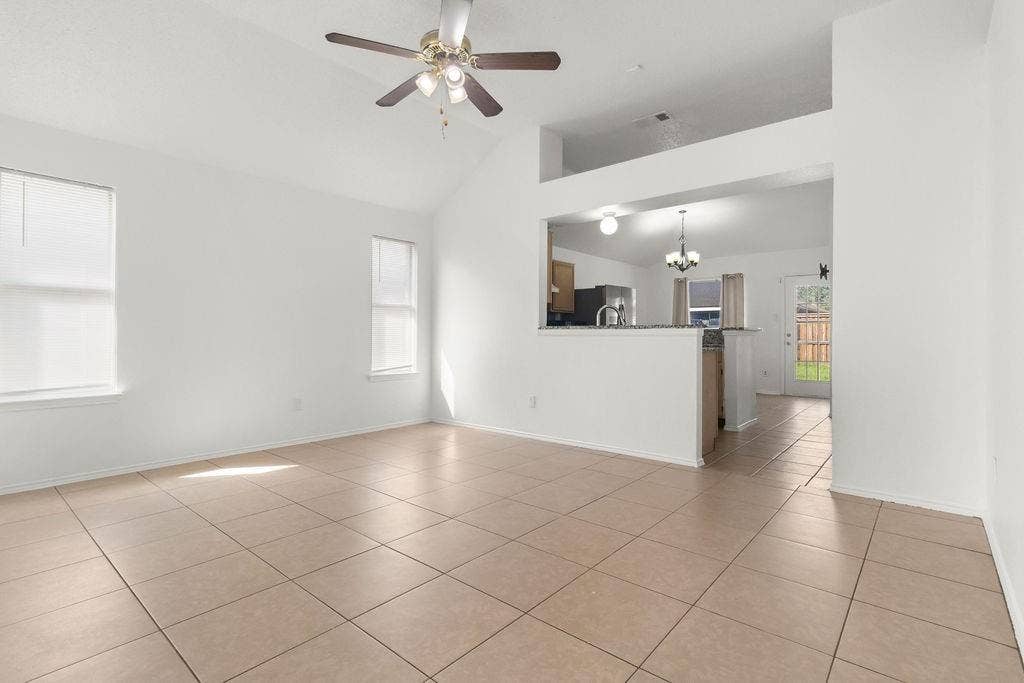 Vaulted ceilings, large-format ceramic tile flooring, ceiling fan with integrated lighting, and a breakfast bar counter