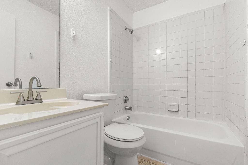 Bathroom featuring a white vanity with an integrated countertop sink, polished chrome faucet, full-width mirror, and a shower-tub combination with white tile surround