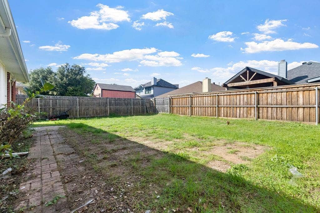 Backyard featuring a grass lawn, perimeter wood fencing, and a brick paver walkway