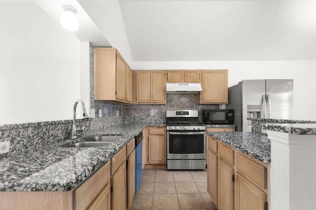 Kitchen featuring wood cabinetry, stone-finish countertops, tile flooring, stainless steel appliances, and a vaulted ceiling