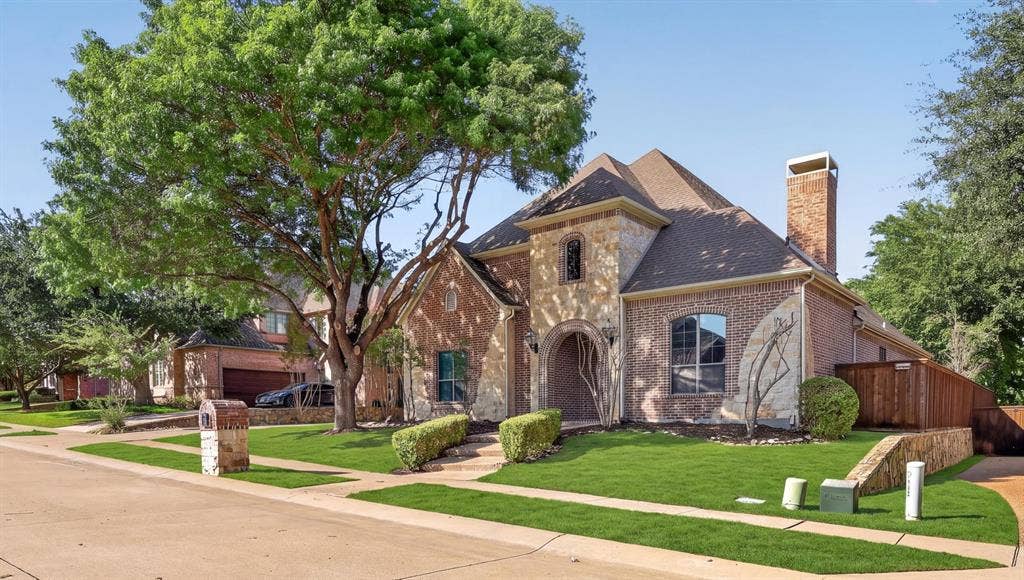 112 Winsley Circle, McKinney, TX 75071 3 car garage, brick and stone facade, arched entryway, gabled roof, mature tree, and a wooden privacy fence.