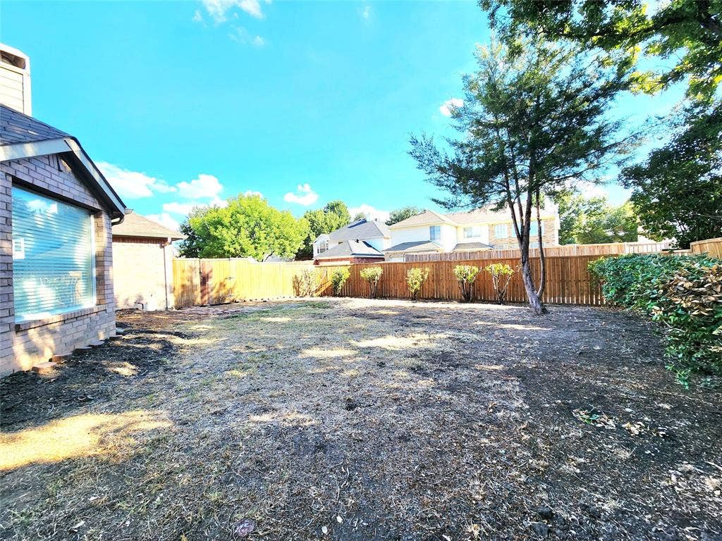 10307 Asheboro Street, Frisco, TX 75035 Expansive backyard featuring a wood fence, mature tree, and a brick exterior with a large window