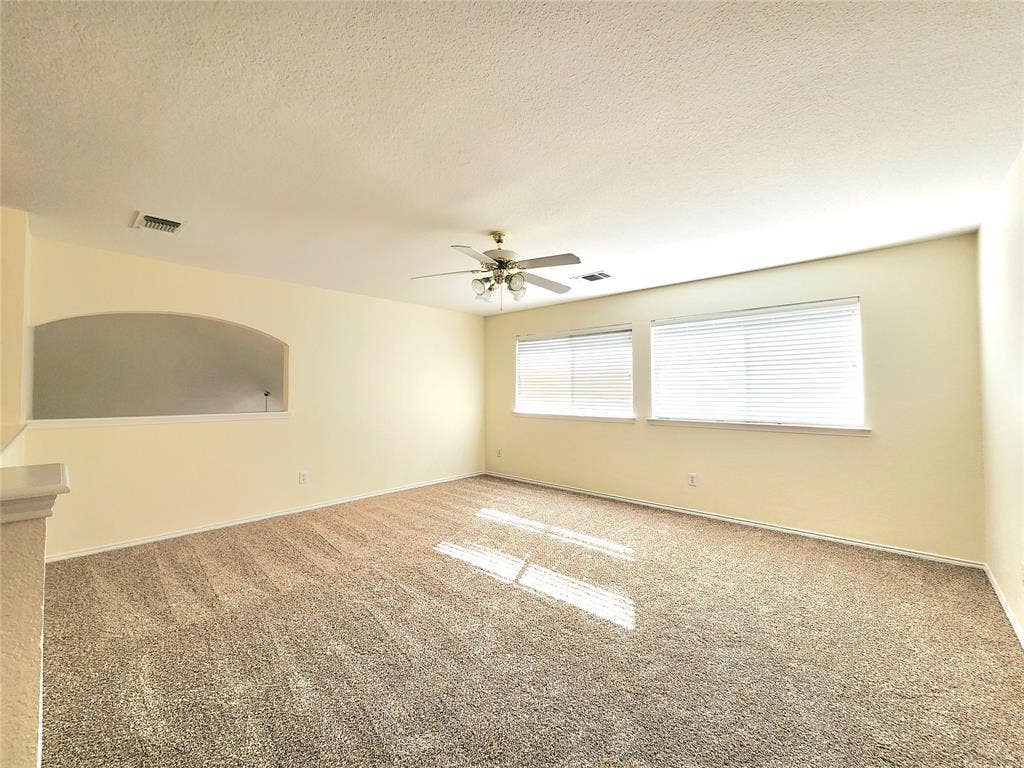10307 Asheboro Street, Frisco, TX 75035 Expansive room featuring carpet flooring, two windows with blinds, a ceiling fan, and an arched wall cutout