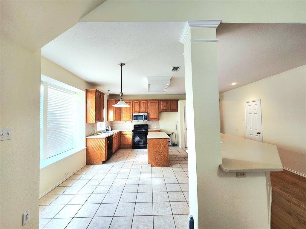 10307 Asheboro Street, Frisco, TX 75035 Kitchen featuring wood cabinetry, white tile flooring, stainless steel microwave, black electric range, and a breakfast bar