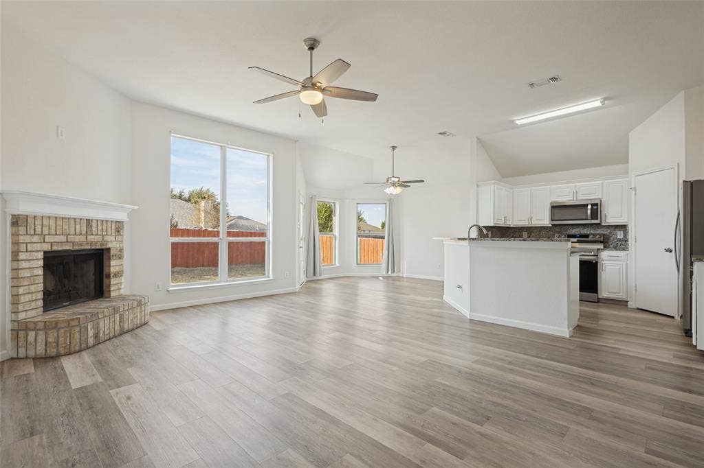 2405 Collier Drive, McKinney, TX 75071 Spacious living area featuring light wood-finish flooring, a brick fireplace, and vaulted ceilings