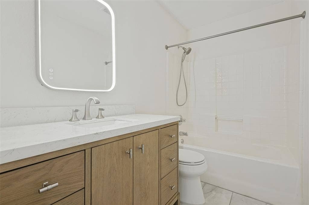 2405 Collier Drive, McKinney, TX 75071 Bathroom featuring a white bathtub with a shower head, wood-finish vanity with a white countertop, and a lighted mirror