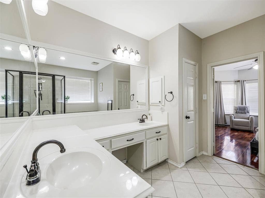 1206 Bel Air Drive, Allen, TX 75013 Dual vanity with integral sinks, white cabinetry, dark bronze fixtures, and an expansive mirror