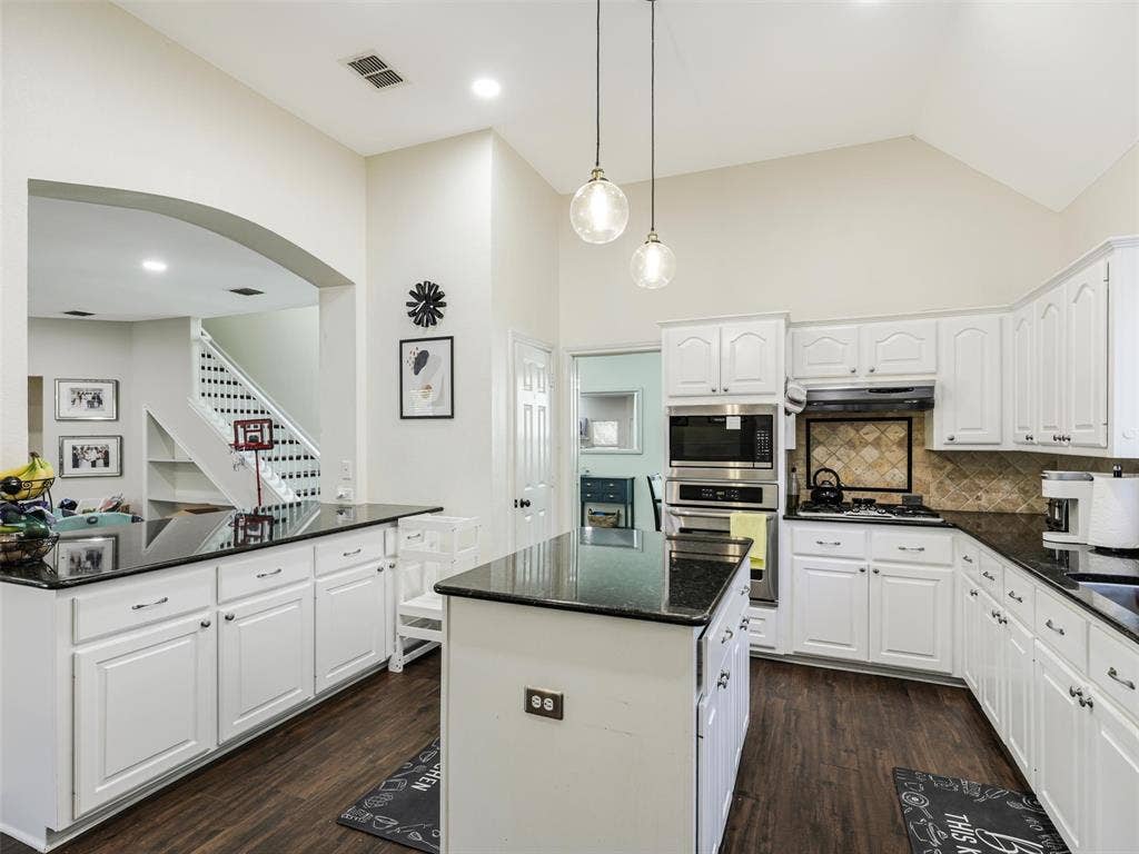 1206 Bel Air Drive, Allen, TX 75013 Kitchen featuring white cabinetry, dark countertops, wood-finish flooring, stainless steel appliances, and a vaulted ceiling