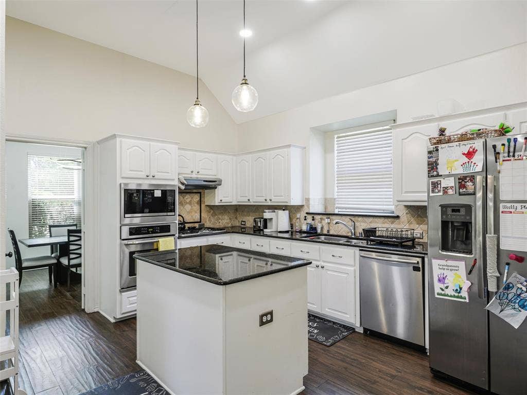 1206 Bel Air Drive, Allen, TX 75013 Kitchen featuring vaulted ceilings, white cabinetry, a center island with a dark countertop, stainless steel appliances, and wood-finish flooring