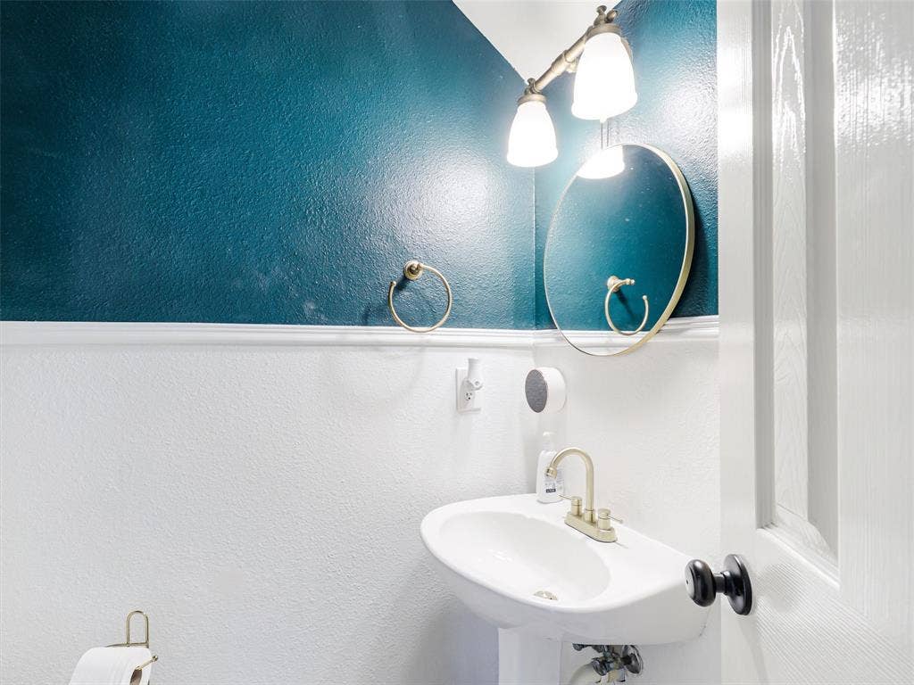 1206 Bel Air Drive, Allen, TX 75013 Pedestal sink with brass-finish faucet, circular mirror, and wall-mounted vanity light